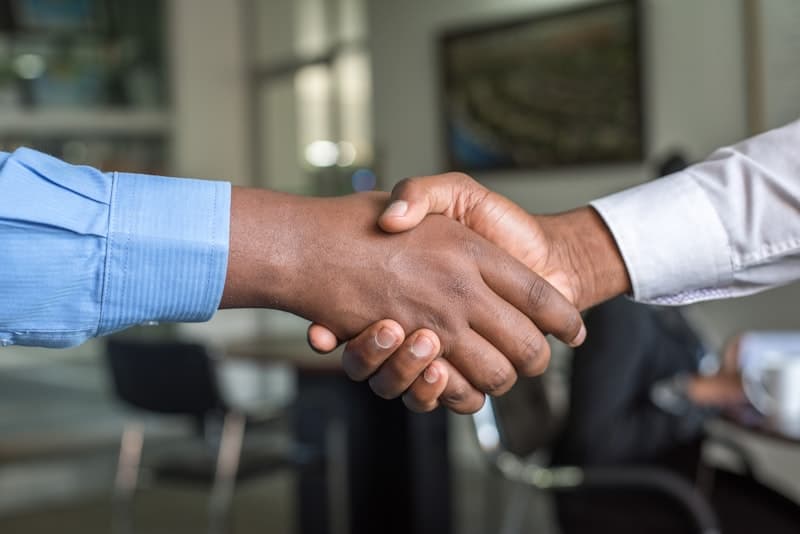 Two people shaking hands across a desk in an office