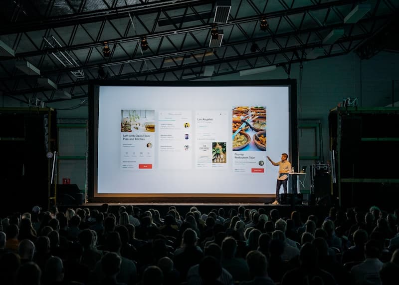 Presenter on stage in front of a large screen and audience